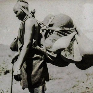 A gîkûyû woman with a load suspended using a head strap.‬